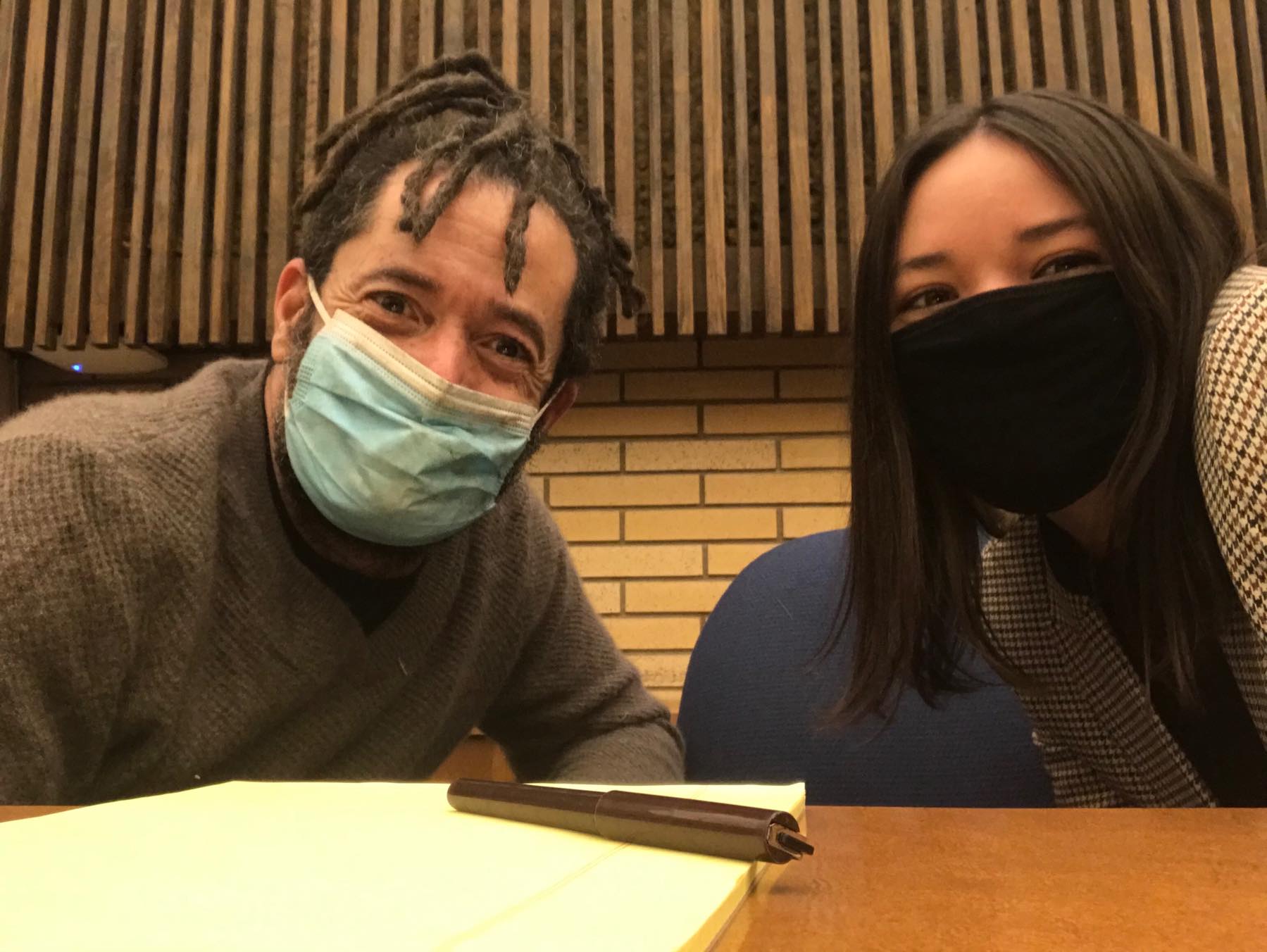 CLDC client Eric Jackson (l) with CLDC staff attorney Sarah Alvarez (r) sitting at a wooden tadle with a brick and wood wall in the background. Both are wearing surgical masks.