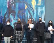 Black Unity members and CLDC lawyers stand in front of a blue and multicolored mural.