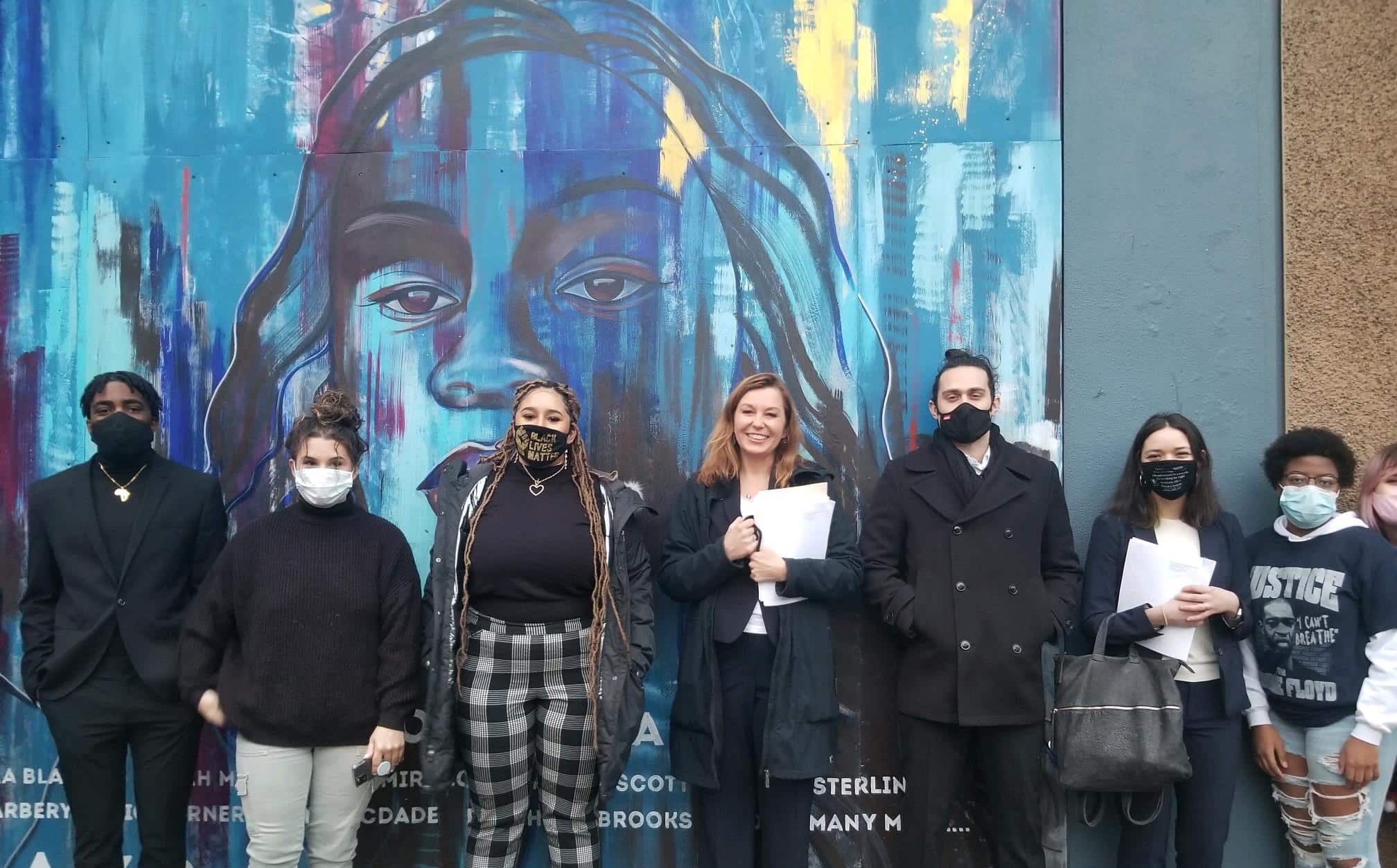 Black Unity members and CLDC lawyers stand in front of a blue and multicolored mural.