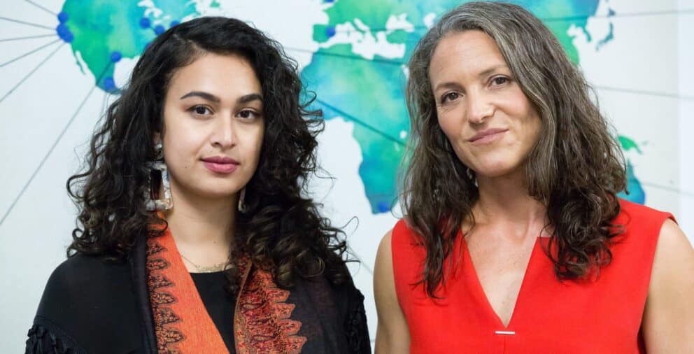 Photo of two femme people, Jasmine Rashid and Morgan Simon, standing in the Candide Group office.