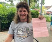 A man with curly brown hair and white complexion smiles while holding a pink parks citation. Text reads: City of Eugene Drops Charges Against Houseless Advocate