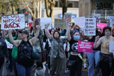 A crowd of people march in the street to protest the leak of a Supreme Court ruling overturning Roe V. Wade. They are raising their fists and holding signs.