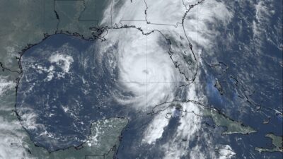 "Satellite image of Hurricane Helene in the Gulf of Mexico. The storm's large, swirling eye is clearly visible as it approaches the coast of Florida. The storm covers much of the Gulf with thick cloud bands extending across Cuba, the Gulf, and part of Florida, indicating the powerful reach of the hurricane."