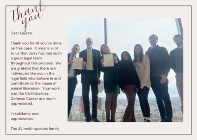 A thank you card with handwritten-style text at the top reading 'Thank you'. The card contains a message addressed to Lauren thanking her for legal work related to Jerry's case and support for animal liberation causes, signed by 'The JV multi-species family'. On the right side is a photo showing a group of people standing together in what appears to be an office or building with a city view through windows behind them. Some individuals in the photo are holding up documents.