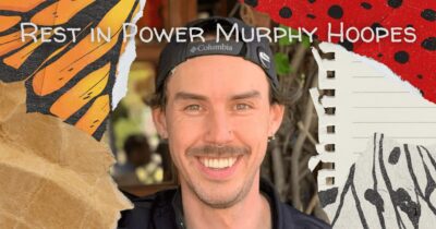 Memorial graphic with "Rest in Power Murphy Hoopes" in white text at top. Portrait photo of Murphy Hoopes, a smiling white man with a mustache wearing a black Columbia cap and black shirt. Background features vibrant orange and red tones with black brushstroke patterns and a partial view of a monarch butterfly wing on the left side. A spiral notebook edge is visible on the right with partial handwritten text.